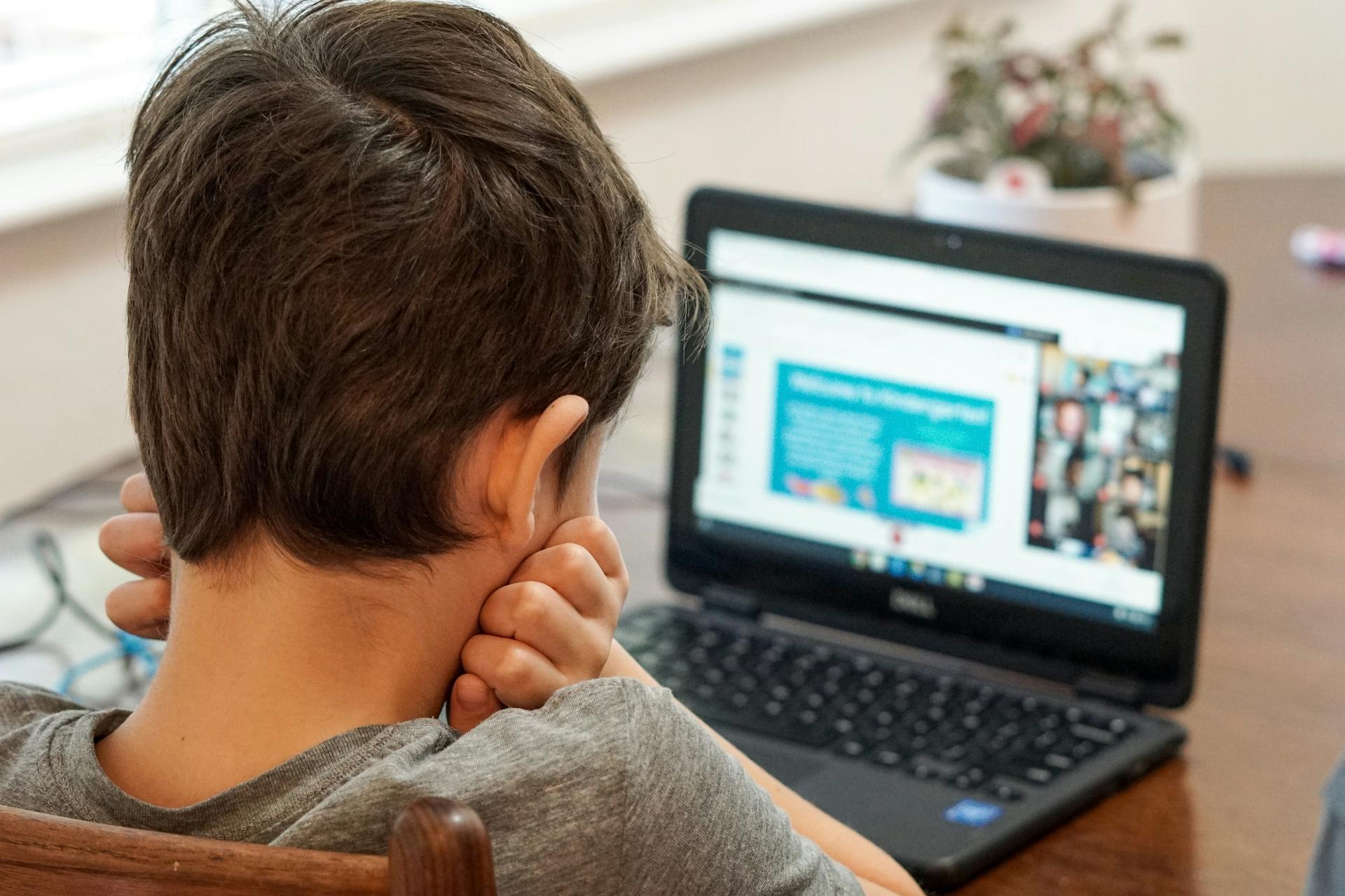 Boy in gray shirt using black laptop computer