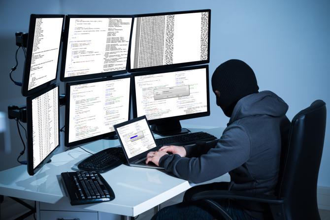 A hacker working on a laptop and many screens in order to steal data